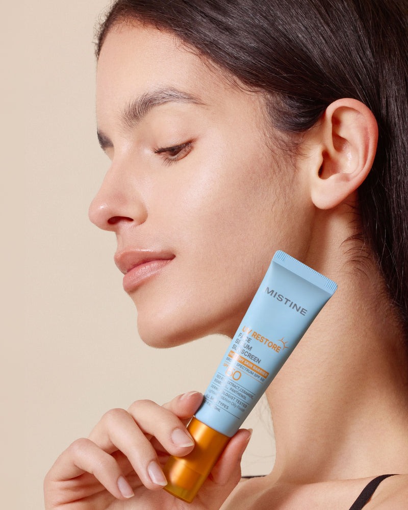 Woman holding a tube of Mistine sunscreen against a beige background